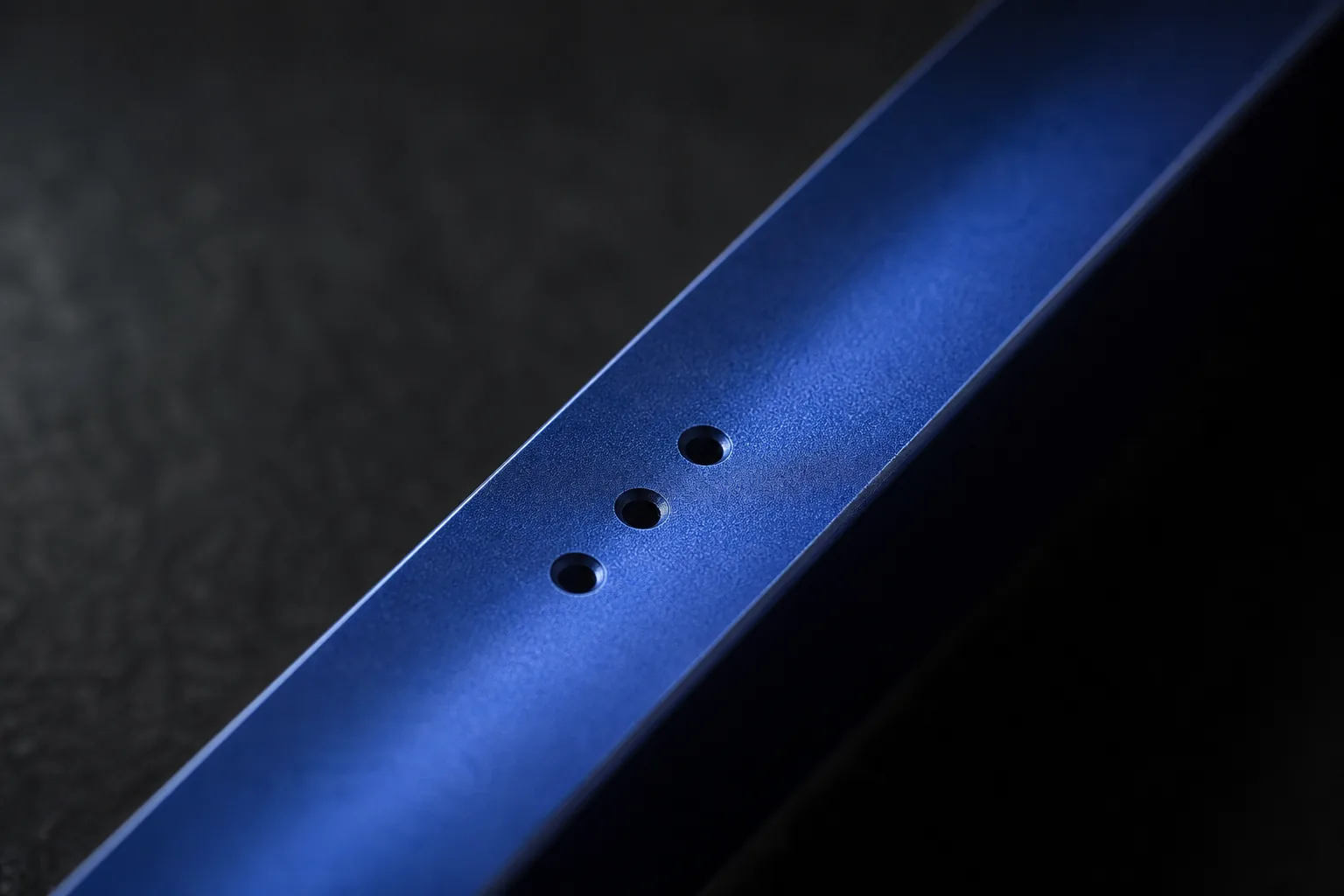 Macro photograph of a deep blue anodized aluminum bar with three drilled holes