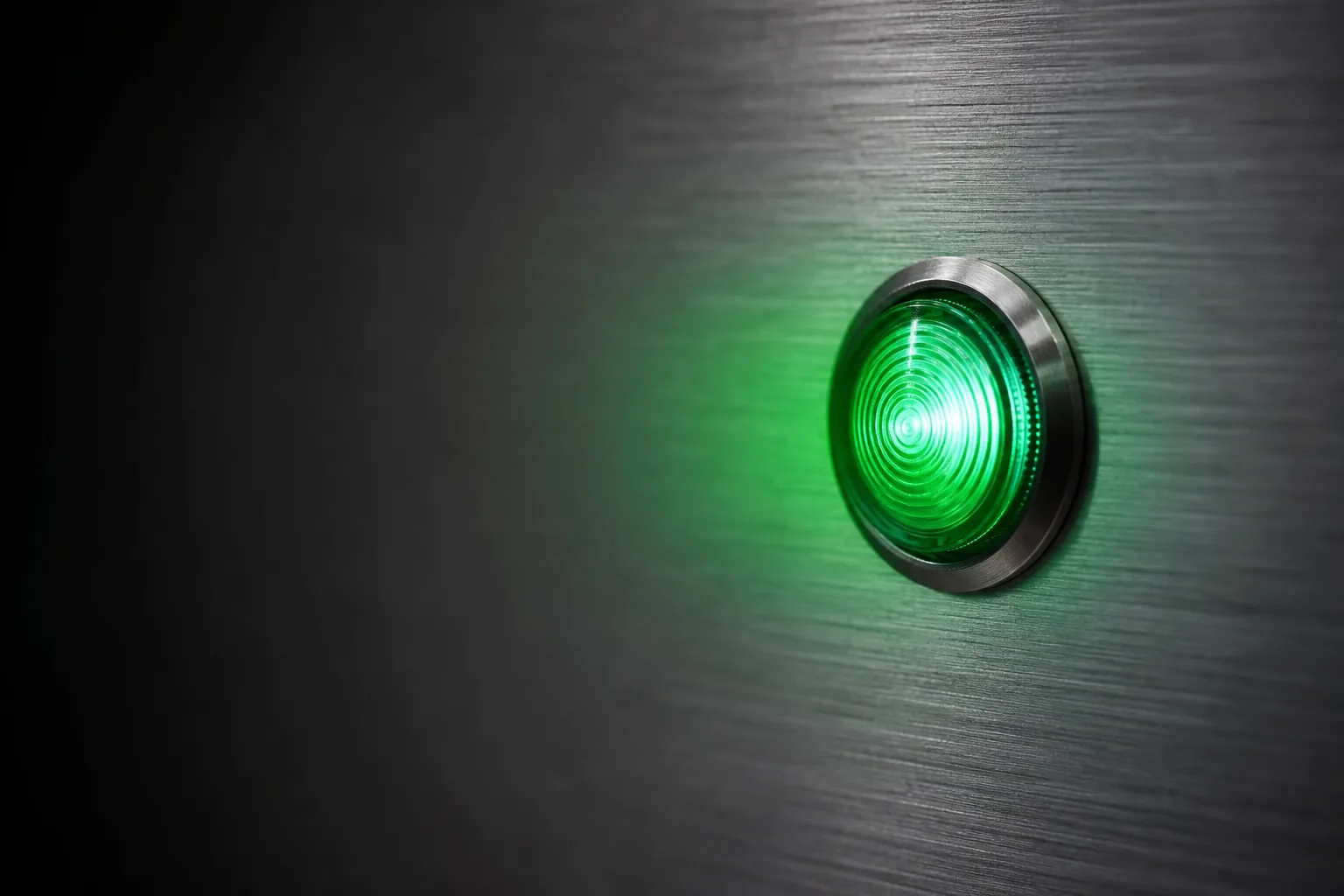 A single emerald indicator lamp glowing softly in a brushed aluminum panel